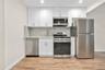 Kitchen featuring stainless steel appliances, white cabinetry, light wood-type flooring, decorative backsplash, and light stone counters