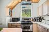 Kitchen featuring wood-paneled sloped ceiling, light-toned cabinetry, light countertops, and a stainless steel electric range
