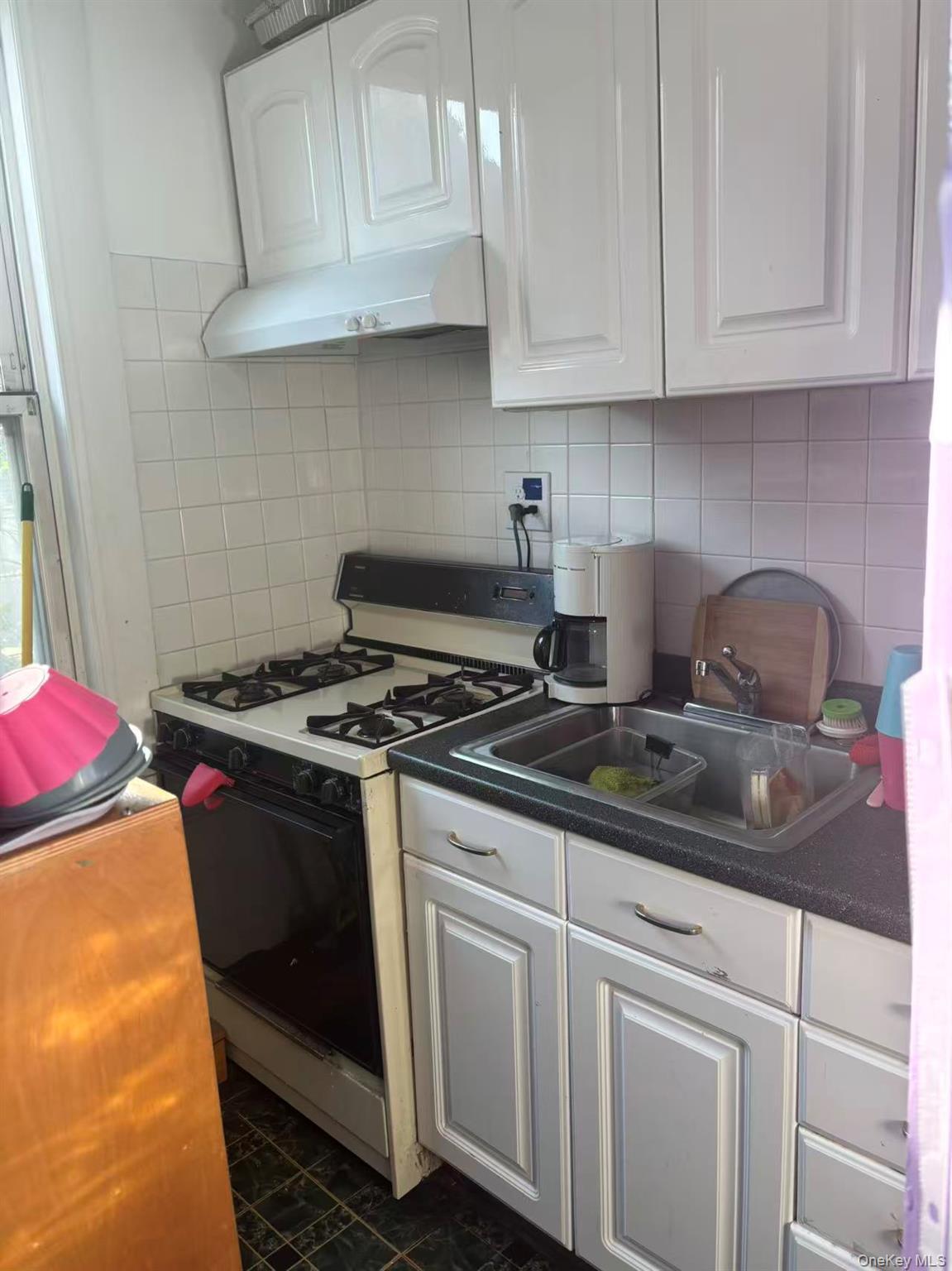 Kitchen with white cabinets, white gas stove, under cabinet range hood, and decorative backsplash