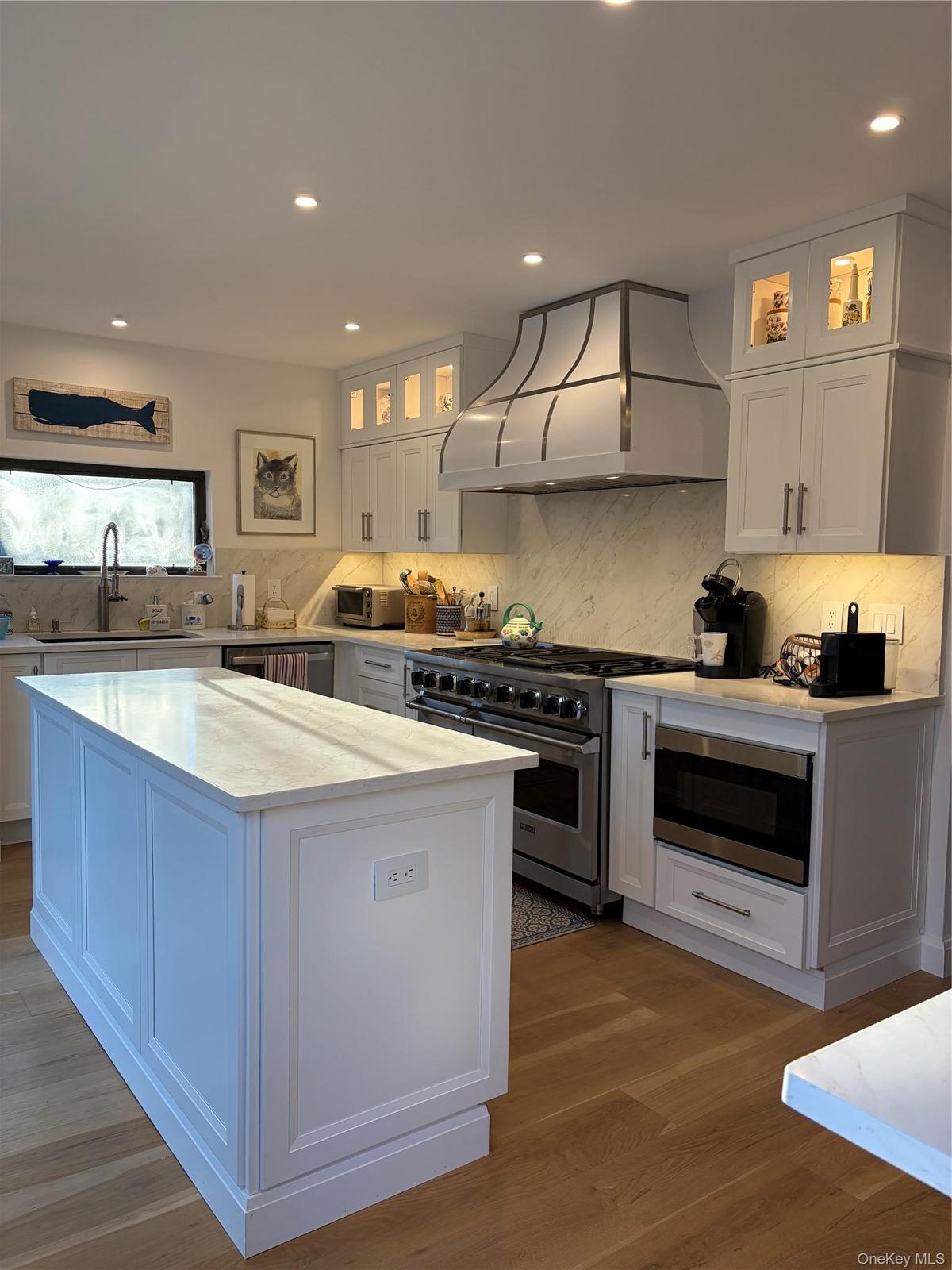Kitchen with glass insert cabinets, stainless steel appliances, dark wood-type flooring, a center island, and white cabinetry