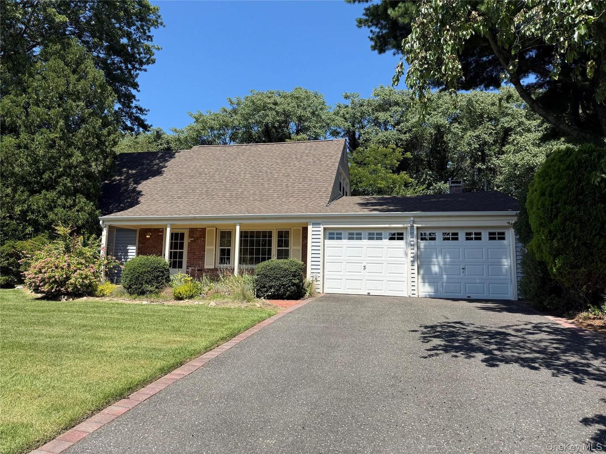 White siding exterior with brick accents, covered front porch, asphalt shingle roof, two-car garage, and a paved driveway with brick edging