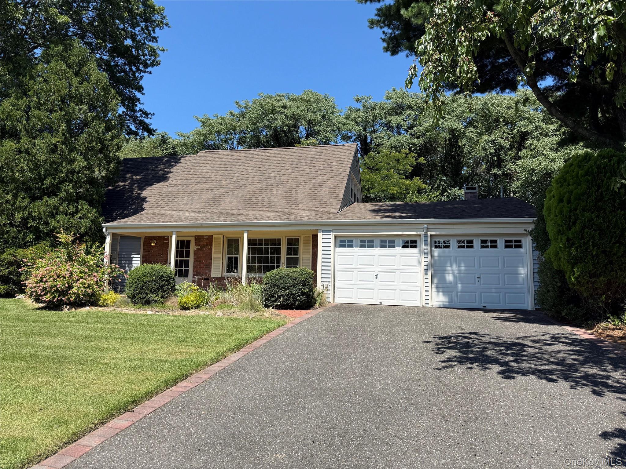 White siding exterior with brick accents, covered front porch, asphalt shingle roof, two-car garage, and a paved driveway with brick edging