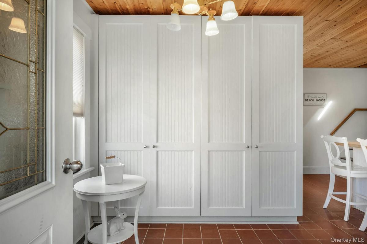 Floor-to-ceiling white beadboard cabinetry with nickel hardware, wood-finish ceiling, and terra cotta tile flooring