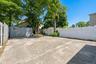 Concrete paved area featuring a detached storage shed with horizontal siding, a white privacy fence, and mature trees