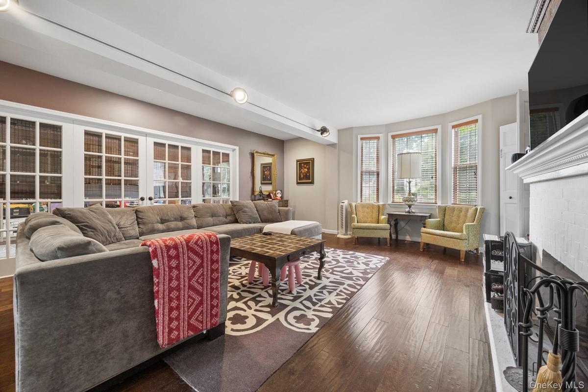 Bright and spacious living room featuring rich hardwood flooring, a wood-burning fireplace, oversized windows, and a charming bay window that fills th