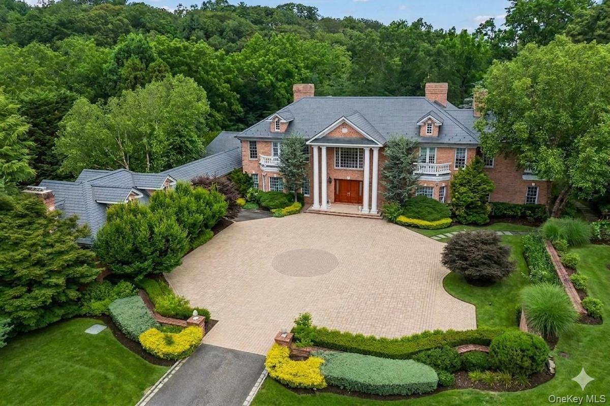 Brick exterior with a prominent portico featuring white columns, a circular paved driveway, and established landscape beds