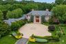 Brick exterior with a prominent portico featuring white columns, a circular paved driveway, and established landscape beds