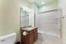 Full bathroom featuring a dark wood-finish vanity with a granite countertop and integrated sink, a large mirror, and a full-size bathtub with a slidin