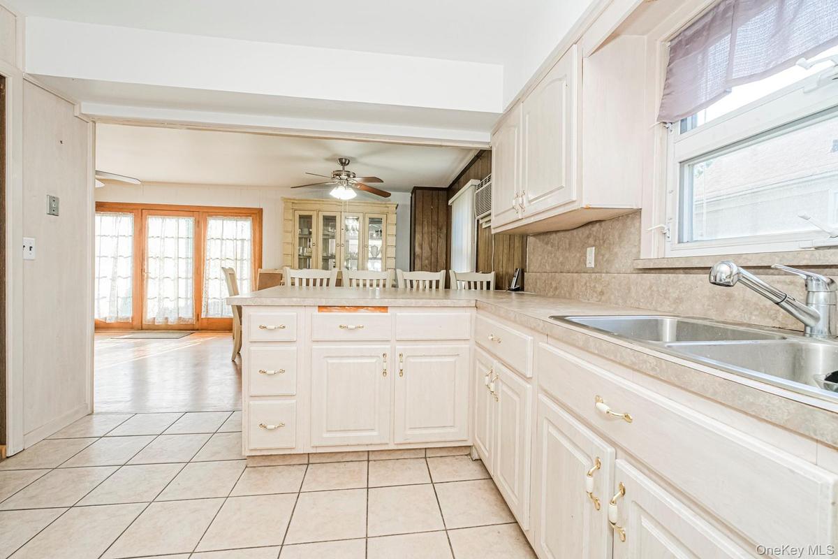 Kitchen featuring tile flooring, white cabinetry, a double basin stainless steel sink with a pull-down faucet, and a light-toned countertop with integ