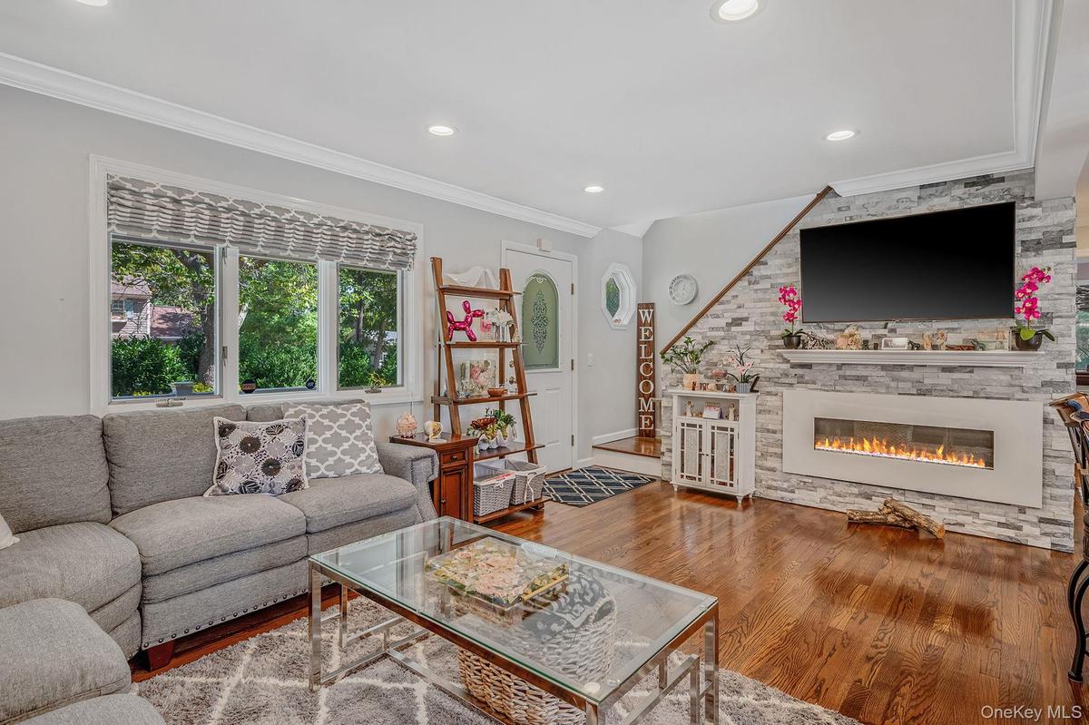 Living room with crown molding, wood finished floors, recessed lighting, and a stone fireplace