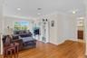 Bright, open living area showcasing hardwood flooring throughout, abundant natural light from large windows, white cabinetry with shelving and media s