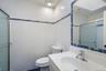 Bathroom featuring white textured wall tiles with a blue decorative band, a white vanity with an integrated sink, a chrome faucet, a framed mirror wit