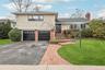 Tri-level home featuring a front yard, driveway, brick siding, a garage, and a chimney