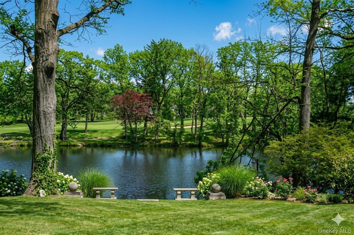 Expansive green lawn bordering a serene body of water, framed by mature trees and lush landscaping