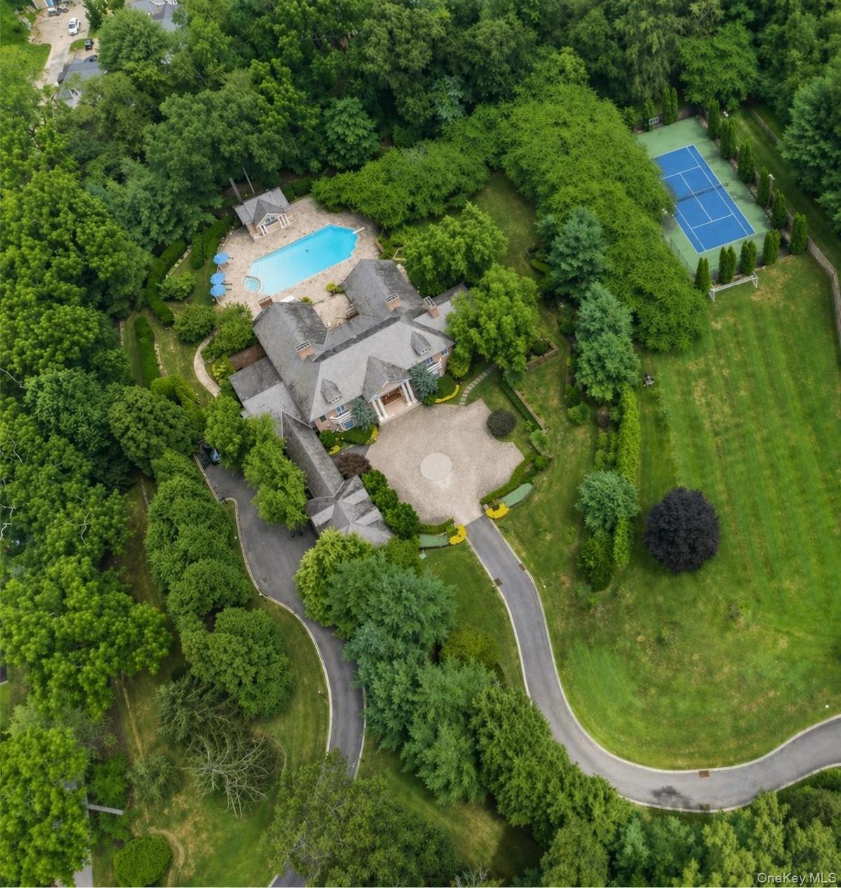 Expansive estate featuring a large swimming pool, paved patio areas, and a full-size tennis court