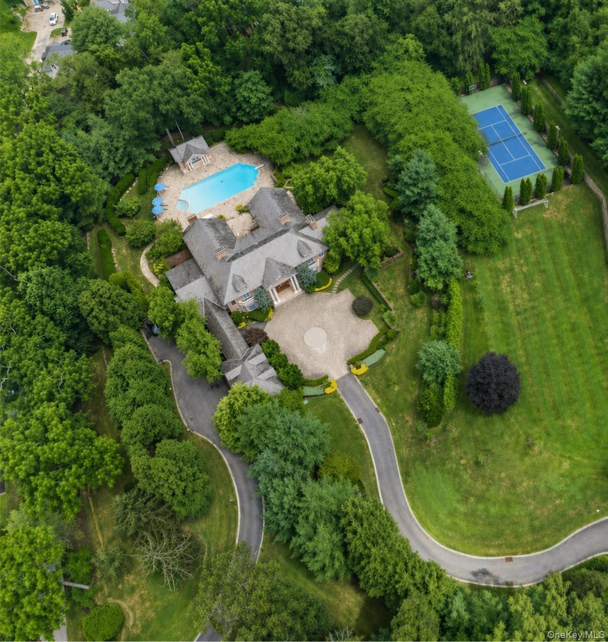 Expansive estate featuring a large swimming pool, paved patio areas, and a full-size tennis court