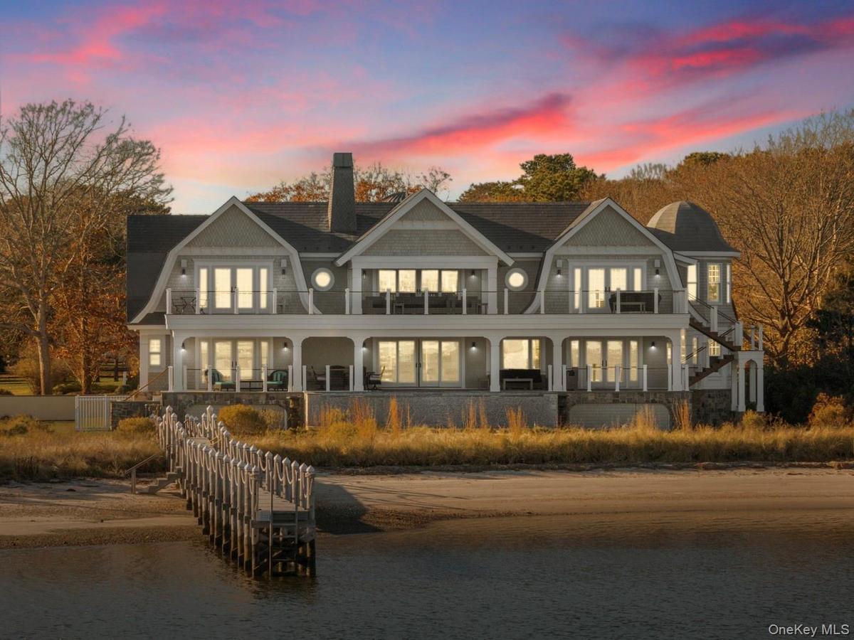 Back of house at dusk featuring a gambrel roof, a chimney, stairs, and covered porch