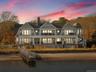 Back of house at dusk featuring a gambrel roof, a chimney, stairs, and covered porch