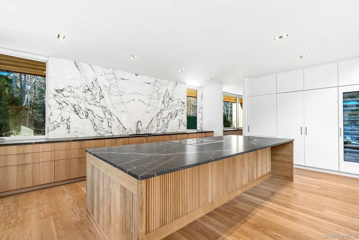 Kitchen with modern cabinets, a large island, beverage cooler, white cabinets, and dark stone counters