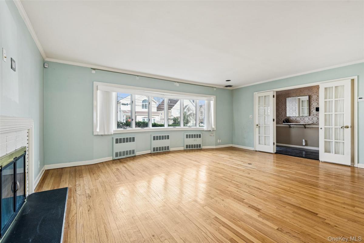 Unfurnished living room featuring a glass covered fireplace, crown molding, light wood-type flooring, french doors, and radiator
