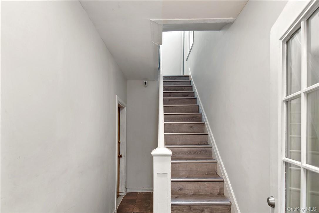 Staircase featuring wood-finish treads and white risers, framed by a white newel post and handrail