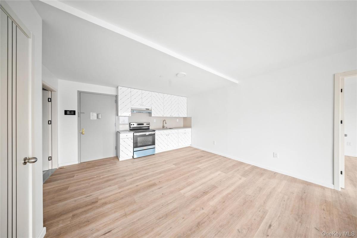 Kitchen featuring white cabinetry, stainless steel range with electric cooktop, light countertops, light wood-type flooring, and open floor plan