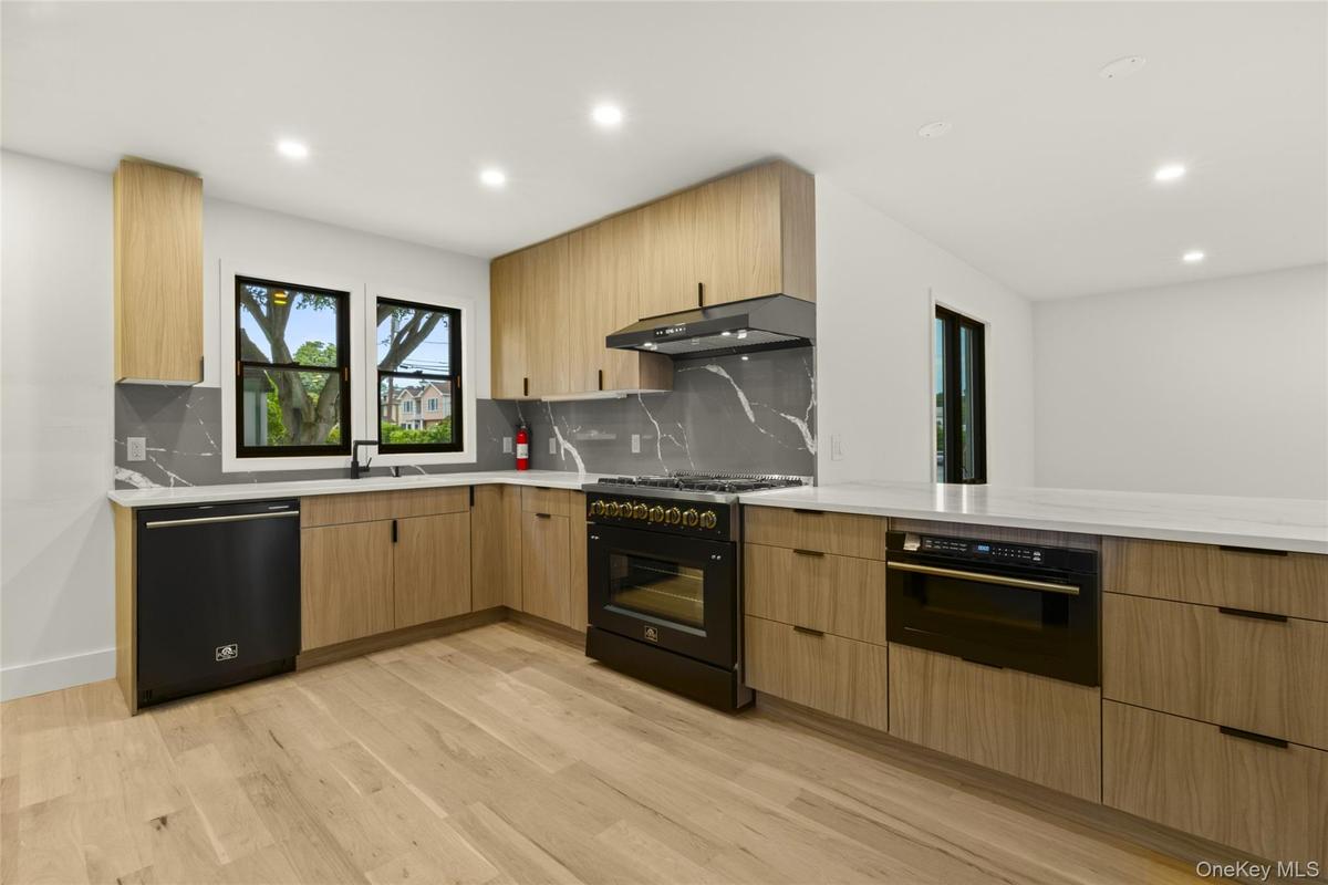 Modern kitchen featuring light wood-finish cabinetry, solid surface countertops, and a full-height stone-look backsplash