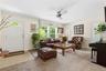 Light-filled living area featuring a white paneled entry door with an arched transom window, large picture windows, a ceiling fan with integrated ligh