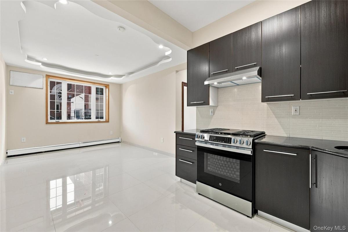 Recessed ceiling lighting, wood-framed window, sleek dark cabinetry, stainless steel range, and tile backsplash