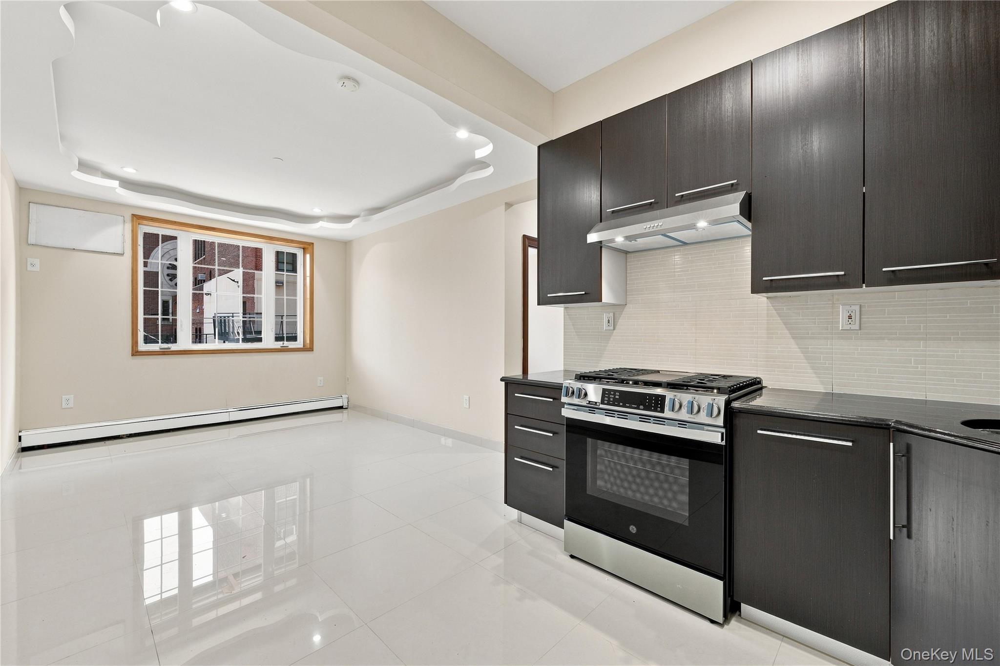 Recessed ceiling lighting, wood-framed window, sleek dark cabinetry, stainless steel range, and tile backsplash