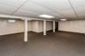 Expansive finished basement featuring carpet flooring, white paneled walls, and a drop ceiling with integrated lighting, zoned baseboard heat