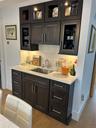 Bar with glass fronted cabinets, light stone countertops, light wood-style floors, and decorative backsplash