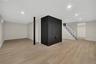 Expansive finished basement featuring wood-finish flooring, recessed lighting, and a prominent black brick accent wall