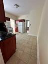 Kitchen featuring dark brown cabinets, refrigerator, range, light tile patterned floors, and extractor fan