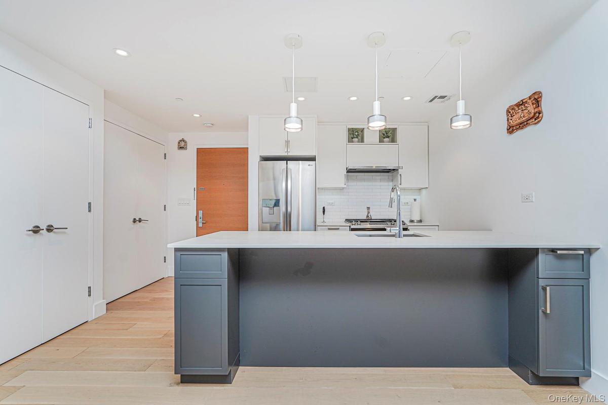 Kitchen with white cabinets, backsplash, gray cabinetry, stainless steel fridge with ice dispenser, and light wood-type flooring