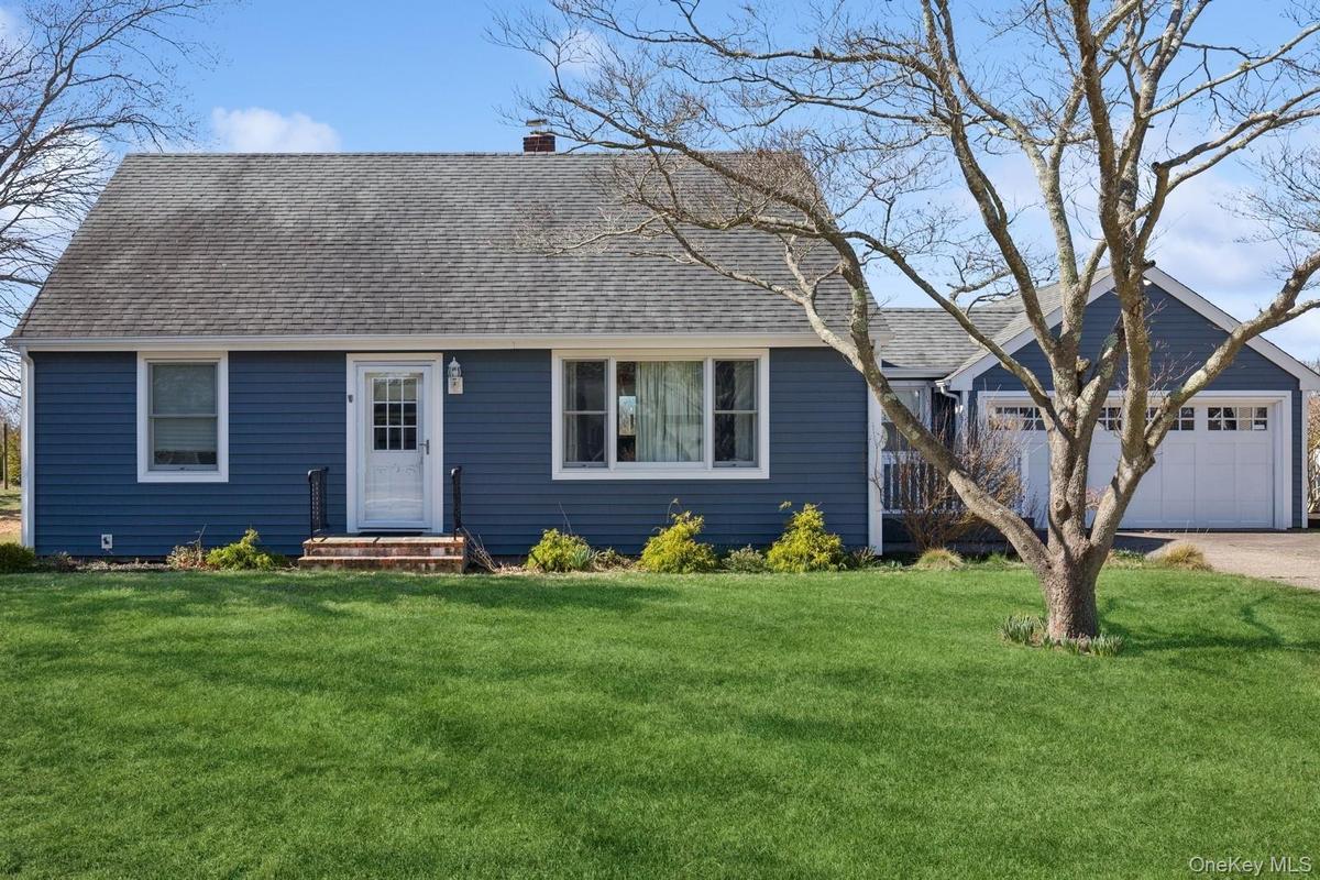 View of front of home featuring a front yard, roof with shingles, a chimney, and a detached garage