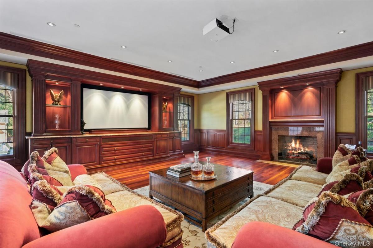 Entertainment room featuring a built-in media center with a projection screen, a wood-burning fireplace with a stone surround, and hardwood flooring