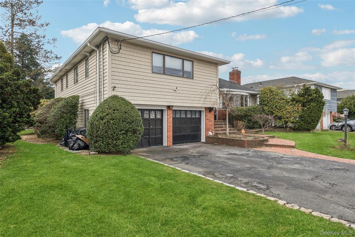 Split level home with a front yard, driveway, a garage, brick siding, and a chimney
