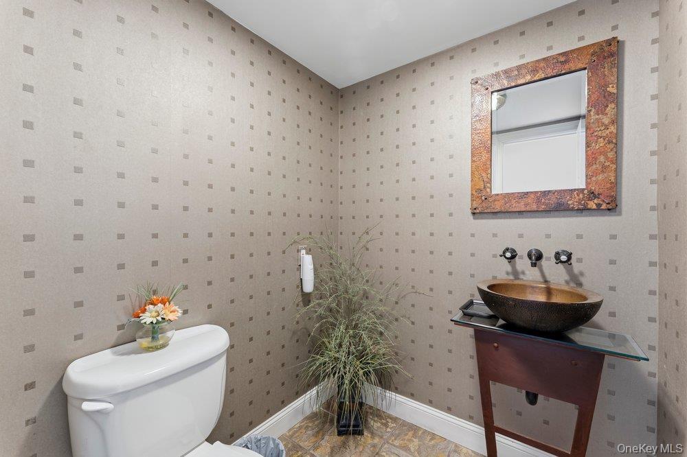 Powder room featuring textured wallpaper, a vessel sink with a wall-mounted faucet, a vanity with a glass top, and tile flooring