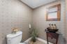 Powder room featuring textured wallpaper, a vessel sink with a wall-mounted faucet, a vanity with a glass top, and tile flooring