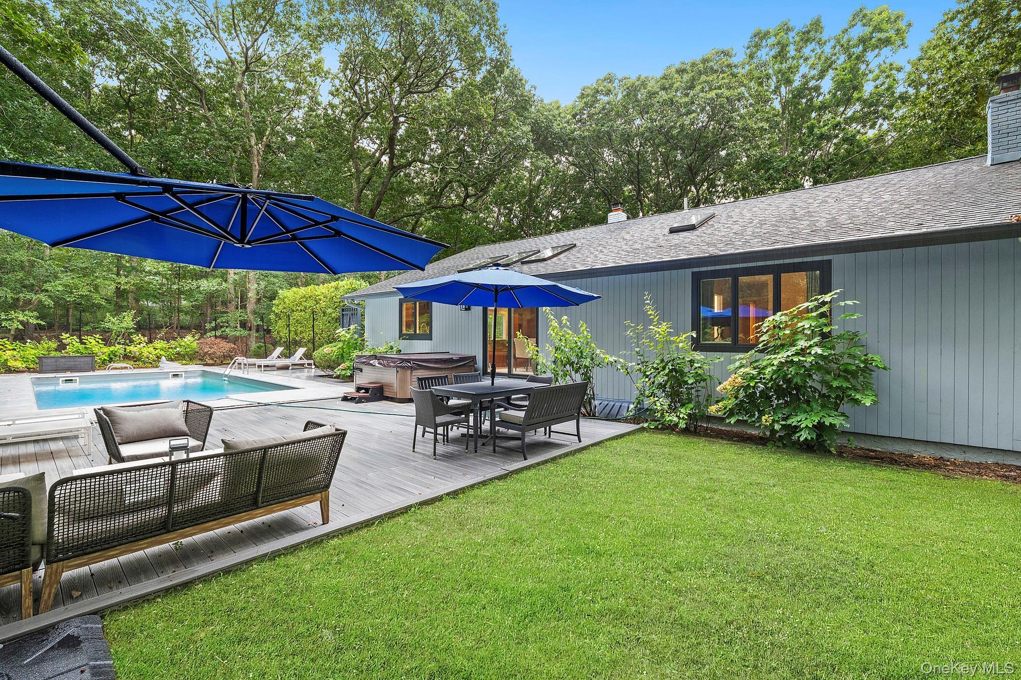 View of grassy yard with a hot tub, a wooden deck, view of scattered trees, and an outdoor pool