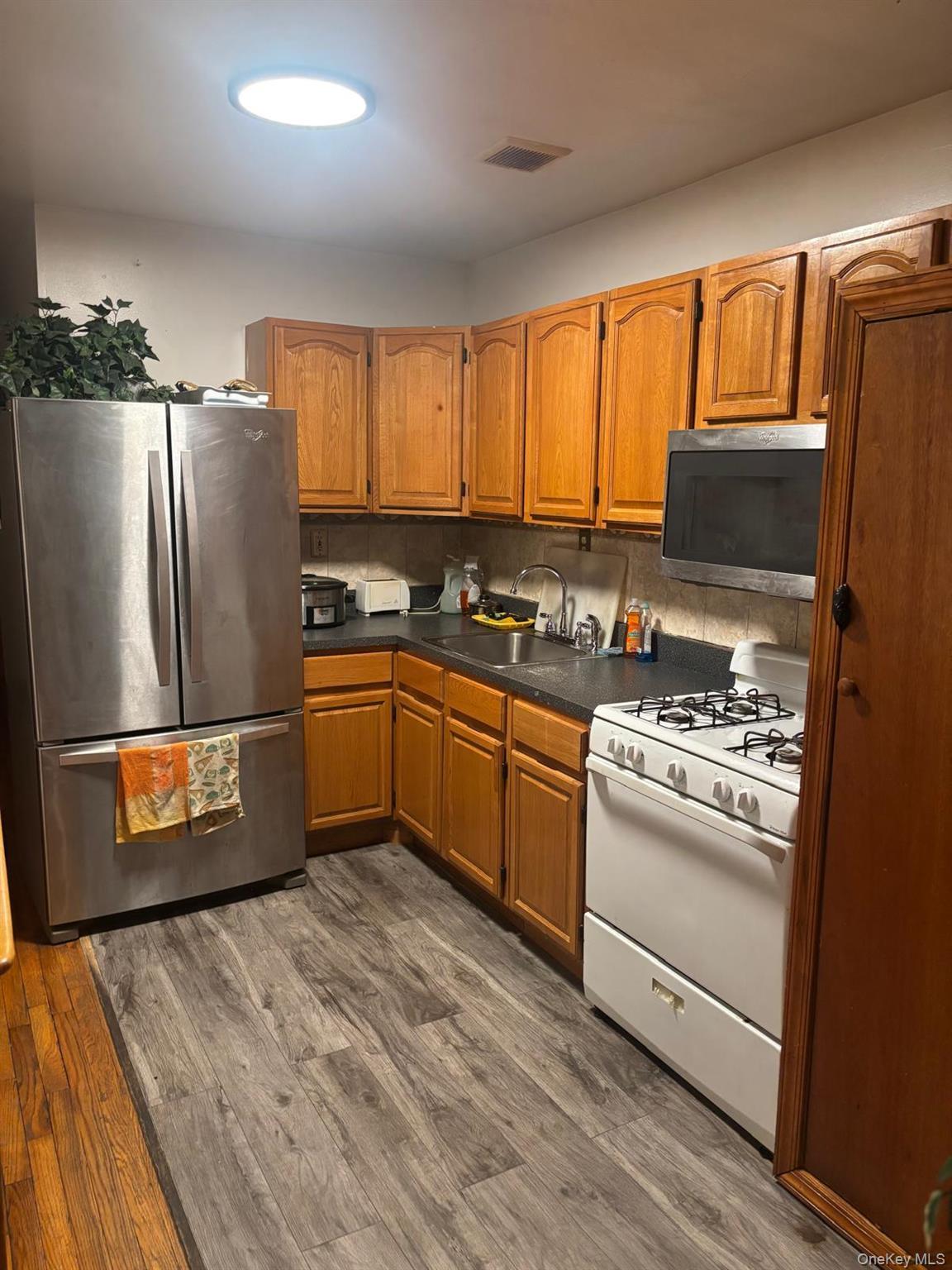 Kitchen with appliances with stainless steel finishes, dark countertops, brown cabinets, tasteful backsplash, and dark wood finished floors