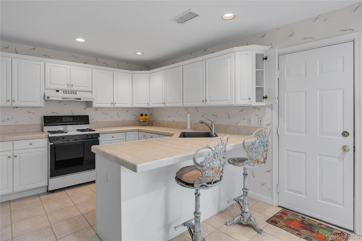 U-shaped kitchen featuring white cabinetry, light-toned countertops, and a black range