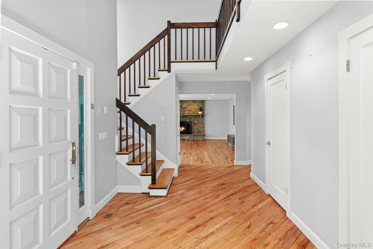 Entrance foyer with light wood-style flooring, baseboards, recessed lighting, stairway, and a stone fireplace