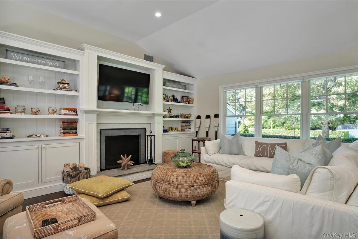 Living room featuring vaulted ceiling, built in shelves, a fireplace with raised hearth, and wood finished floors