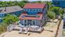 Shingle-sided residence featuring a red gable roof, multiple windows, and a sand-level wood deck