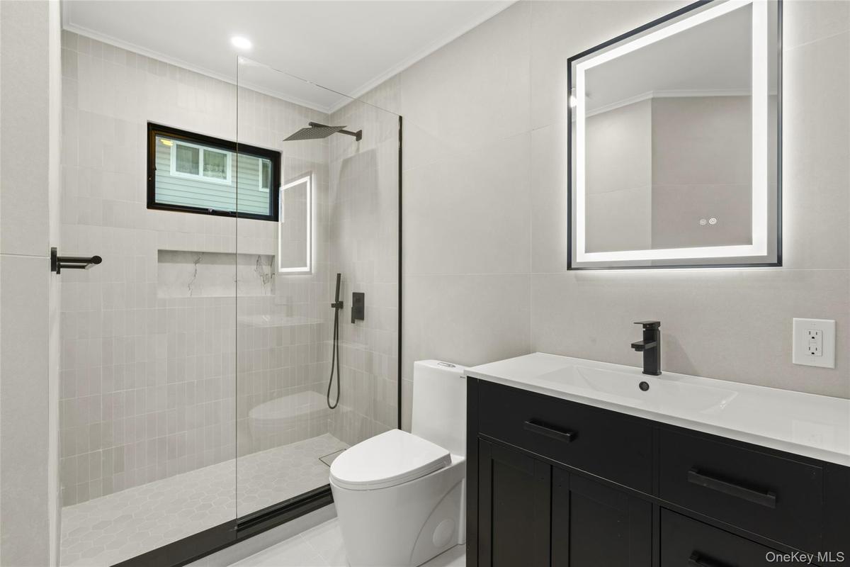 Contemporary bathroom featuring a black framed illuminated mirror, a sleek dark vanity with integrated sink, a glass-enclosed shower with matte black 