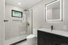 Contemporary bathroom featuring a black framed illuminated mirror, a sleek dark vanity with integrated sink, a glass-enclosed shower with matte black 