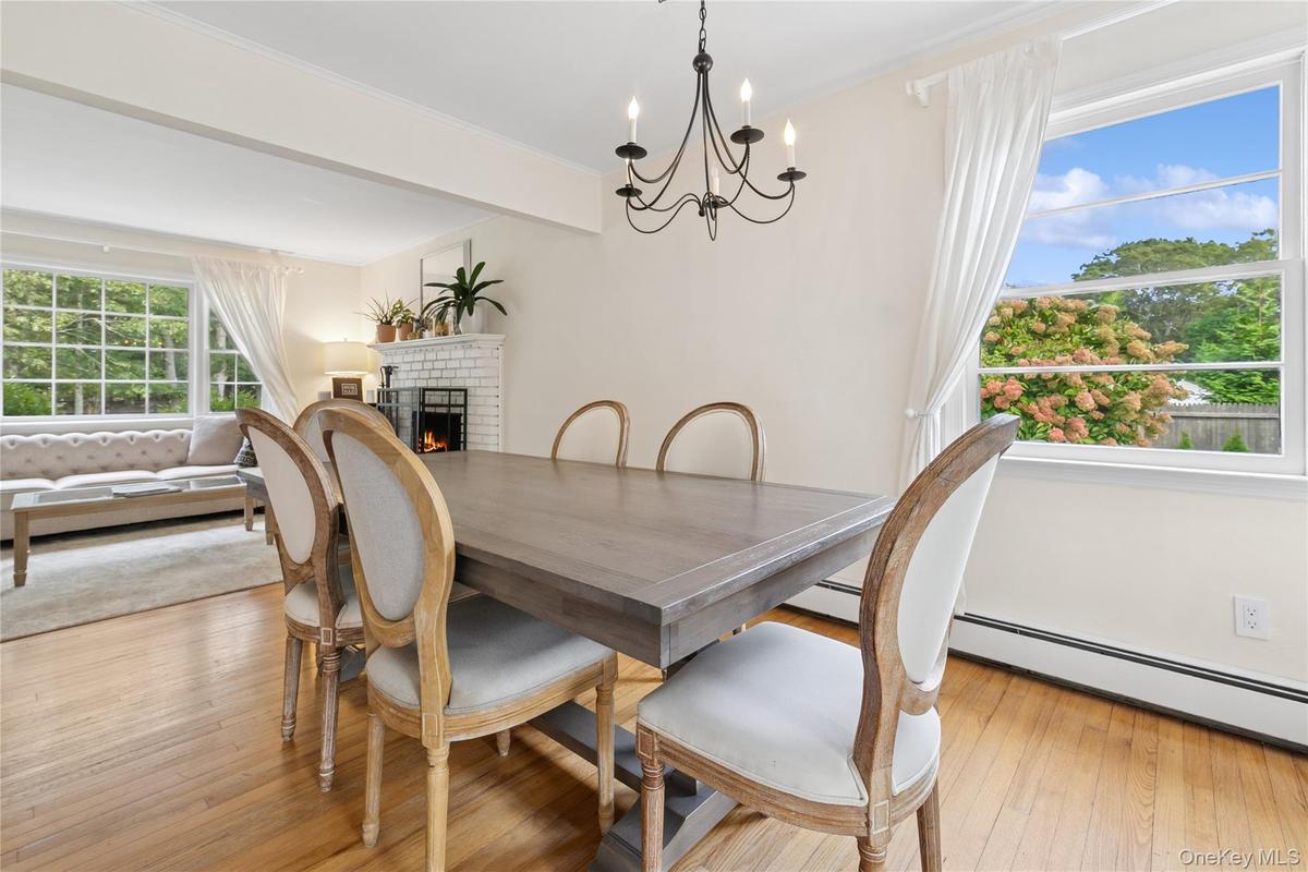 Dining space with a brick fireplace, a chandelier, light wood-type flooring, beamed ceiling, and baseboard heating