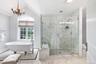 Clawfoot soaking tub, glass-enclosed shower with marble-look tile, arched window, chandelier, and a mosaic tile floor accent